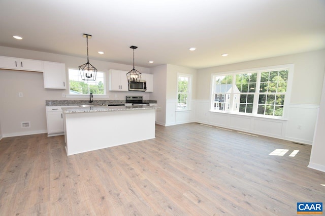 kitchen featuring appliances with stainless steel finishes, white cabinetry, light stone countertops, a kitchen island, and decorative light fixtures