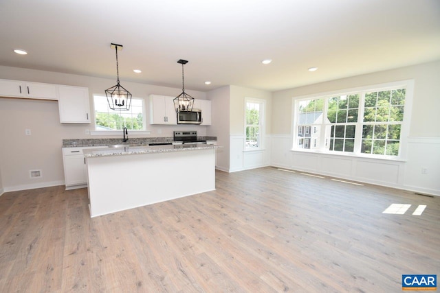 kitchen featuring a kitchen island, appliances with stainless steel finishes, decorative light fixtures, white cabinetry, and light stone countertops