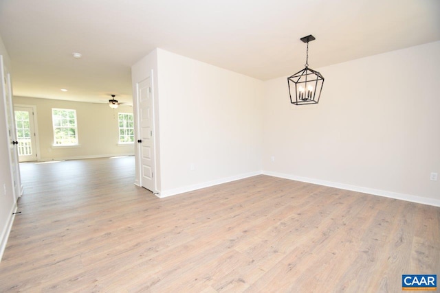 empty room with ceiling fan with notable chandelier and light hardwood / wood-style floors