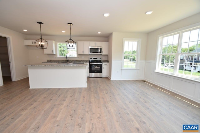 kitchen featuring light hardwood / wood-style flooring, white cabinetry, stainless steel appliances, light stone countertops, and decorative light fixtures