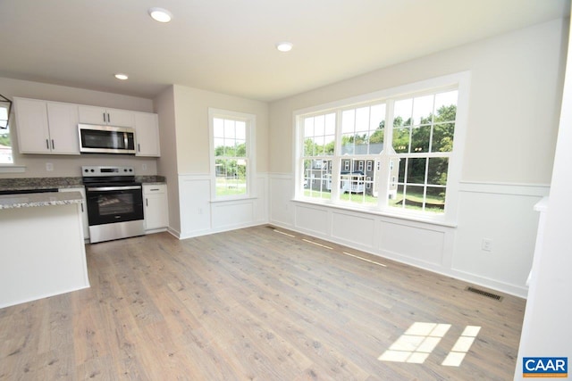 kitchen with stainless steel appliances, white cabinetry, stone counters, and light wood-type flooring