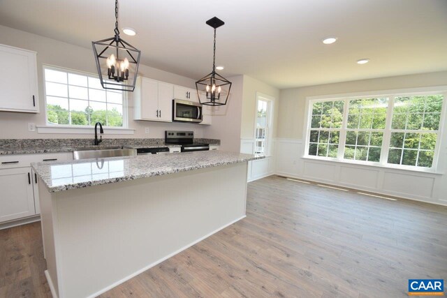 kitchen featuring sink, appliances with stainless steel finishes, white cabinets, a kitchen island, and decorative light fixtures