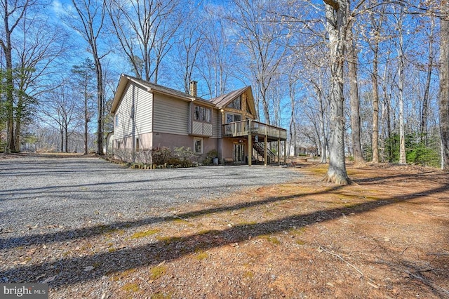 view of side of home featuring driveway, a chimney, a wooden deck, and stairs