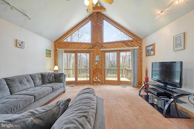 carpeted living room with high vaulted ceiling, rail lighting, ceiling fan, and wooden walls