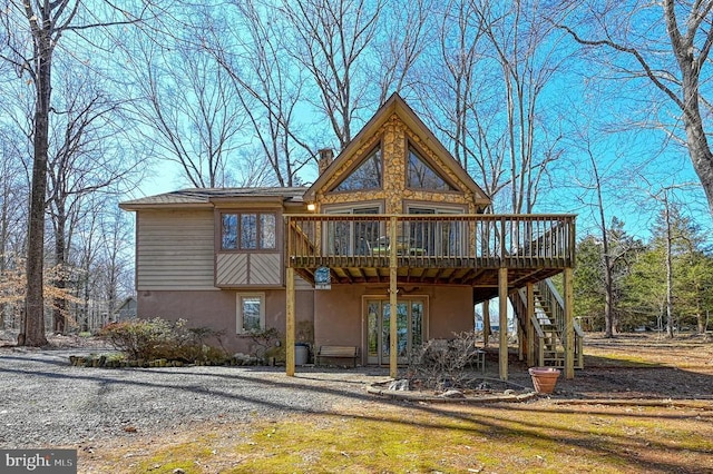 rear view of house featuring a deck, stairway, a chimney, and stucco siding