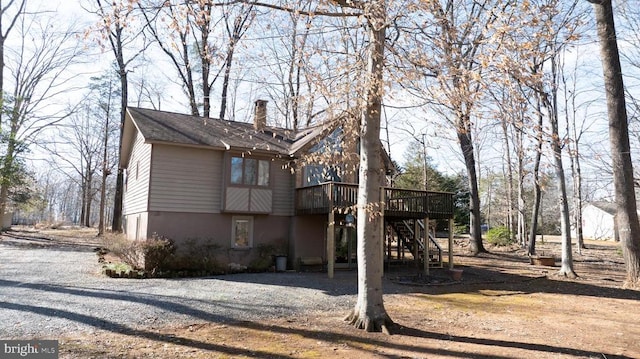 exterior space featuring a chimney, stairway, gravel driveway, a wooden deck, and stucco siding