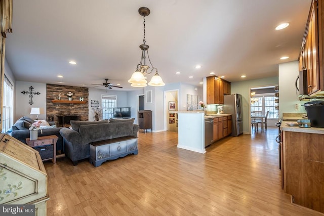 living room featuring a stone fireplace, light hardwood / wood-style flooring, and ceiling fan