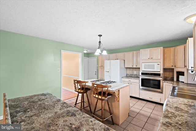 kitchen with white appliances, a breakfast bar, backsplash, a center island, and decorative light fixtures