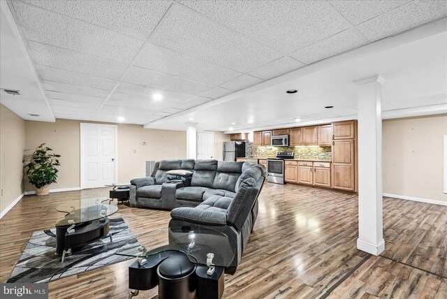 living room featuring hardwood / wood-style flooring, a drop ceiling, and ornate columns