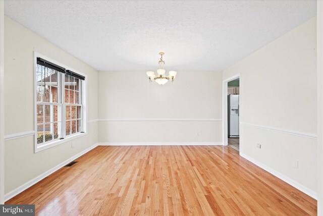 spare room featuring an inviting chandelier, light hardwood / wood-style flooring, and a textured ceiling