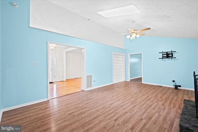 unfurnished living room featuring ceiling fan, hardwood / wood-style flooring, a textured ceiling, and vaulted ceiling with skylight