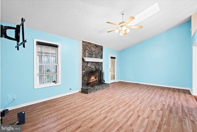 unfurnished living room featuring ceiling fan, lofted ceiling, a stone fireplace, and light wood-type flooring