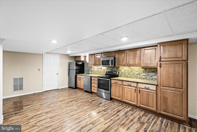 kitchen featuring tasteful backsplash, light stone countertops, stainless steel appliances, and light hardwood / wood-style floors