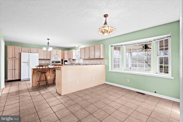 kitchen featuring a breakfast bar area, pendant lighting, backsplash, and white appliances