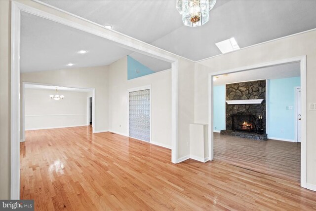 unfurnished living room with an inviting chandelier, wood-type flooring, a stone fireplace, and vaulted ceiling