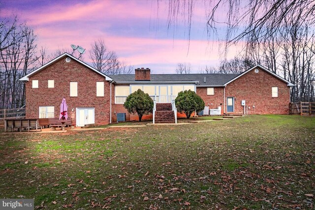 back house at dusk featuring a lawn