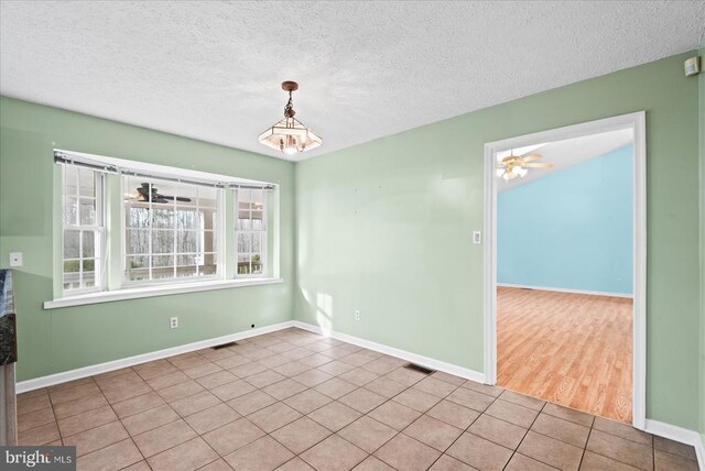 tiled empty room featuring ceiling fan with notable chandelier and a textured ceiling