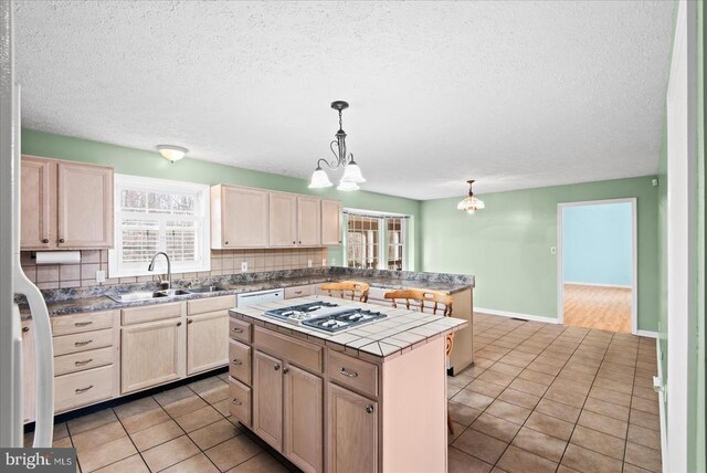 kitchen featuring stainless steel gas cooktop, sink, tile countertops, decorative light fixtures, and a kitchen island