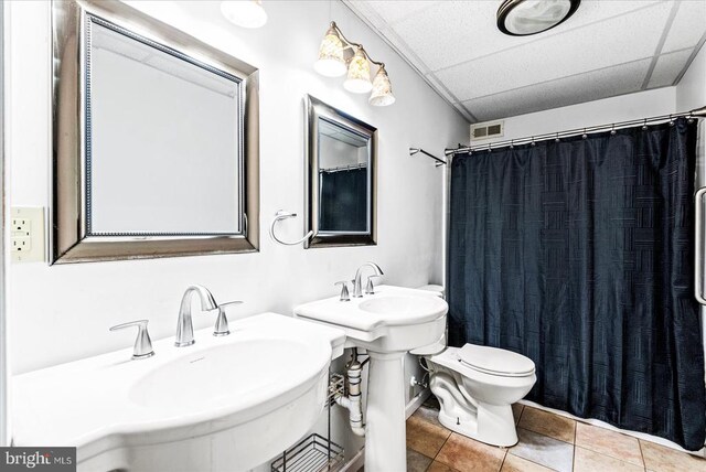 bathroom with double sink, a paneled ceiling, tile patterned floors, and toilet