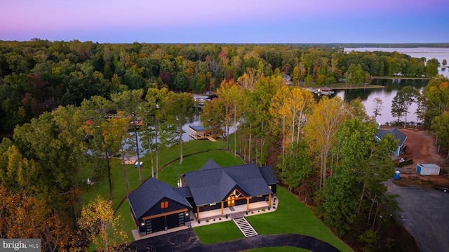 aerial view at dusk with a water view and a view of trees