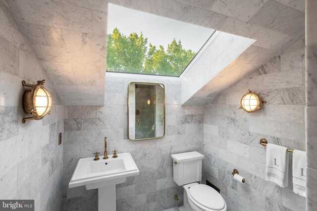 half bath with toilet, tile walls, and a sink