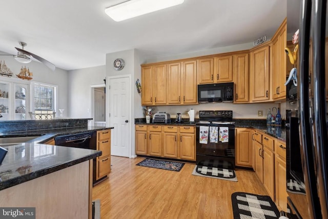 kitchen featuring a ceiling fan, dark stone countertops, light wood-type flooring, black appliances, and a sink