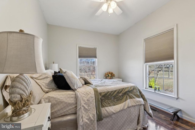 bedroom featuring ceiling fan, multiple windows, baseboards, and wood finished floors