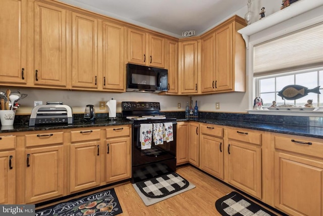 kitchen featuring dark stone countertops, light wood-style flooring, and black appliances