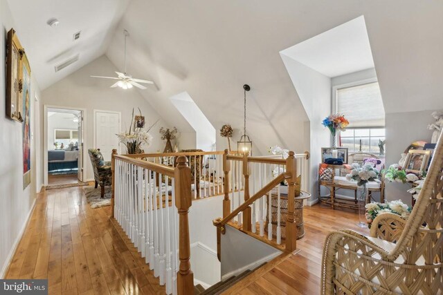 hall with light wood-type flooring, visible vents, lofted ceiling, and an upstairs landing