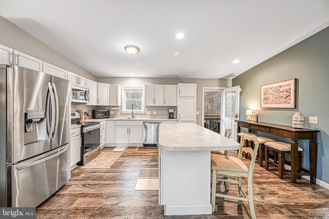 kitchen featuring a center island, a breakfast bar area, stainless steel appliances, light countertops, and a sink