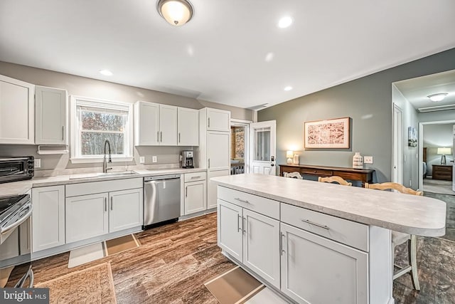 kitchen featuring stainless steel appliances, a sink, white cabinets, a kitchen breakfast bar, and light countertops