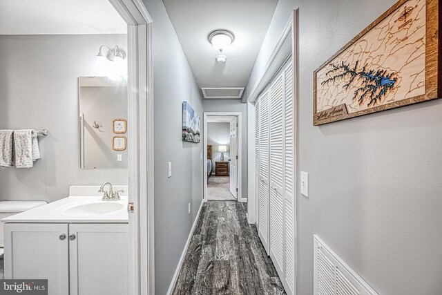 corridor featuring dark wood-style floors, visible vents, attic access, a sink, and baseboards