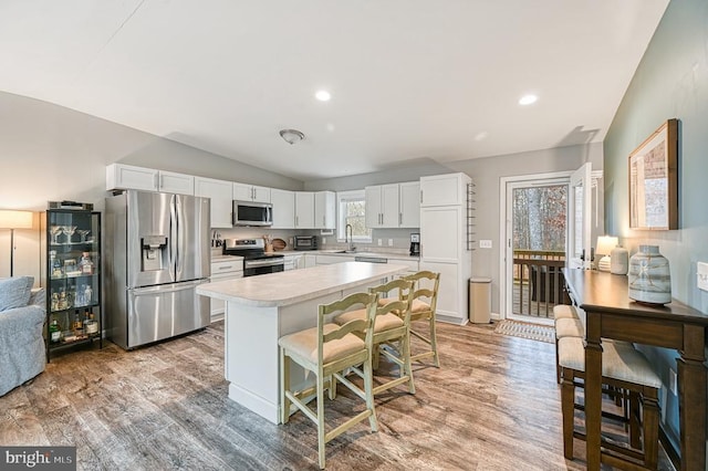 kitchen with light wood-style flooring, stainless steel appliances, a sink, vaulted ceiling, and light countertops