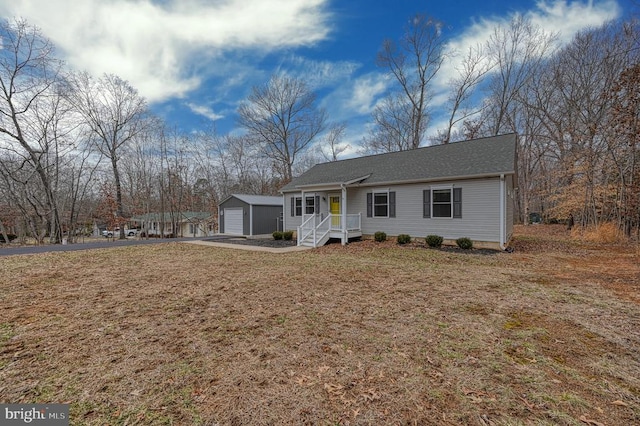 single story home featuring an outbuilding, aphalt driveway, a detached garage, and a front yard