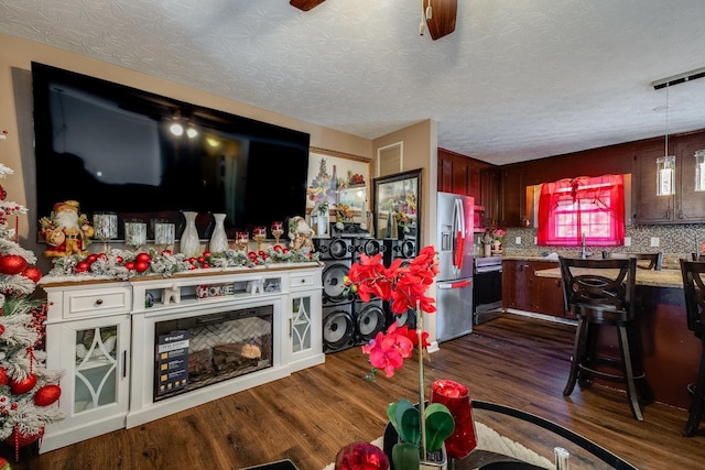 interior space with dark wood-type flooring, a textured ceiling, pendant lighting, stainless steel appliances, and decorative backsplash