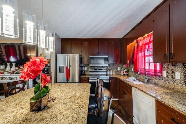 kitchen featuring appliances with stainless steel finishes, a breakfast bar, tasteful backsplash, sink, and hanging light fixtures