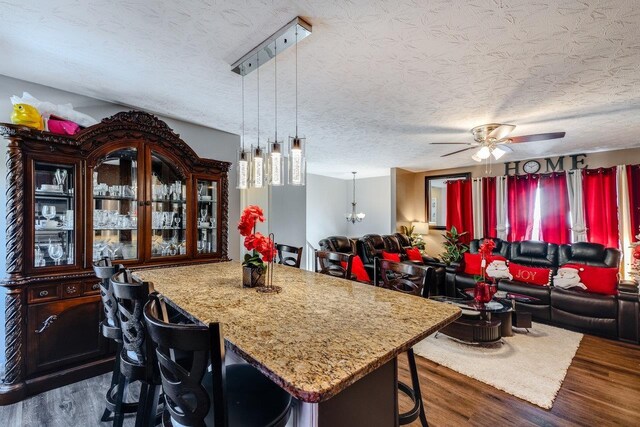 kitchen with dark wood-type flooring, a kitchen bar, a center island, pendant lighting, and ceiling fan