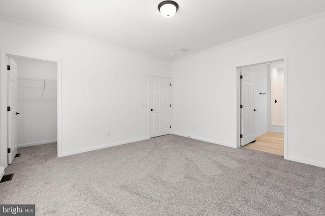 unfurnished bedroom featuring carpet flooring, a closet, crown molding, a walk in closet, and baseboards