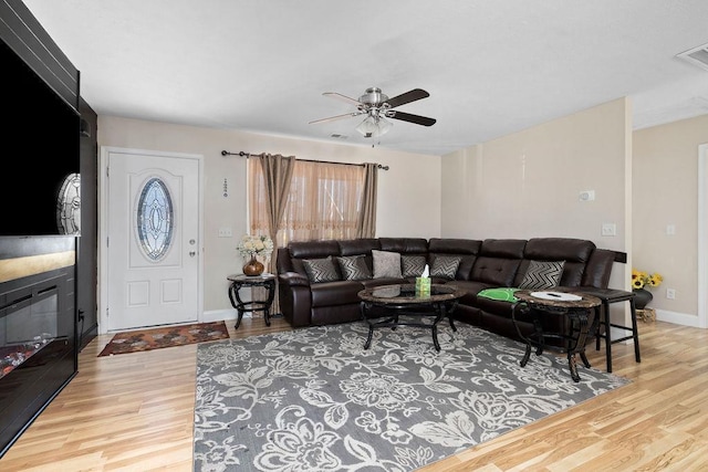 living room featuring a large fireplace, wood finished floors, visible vents, a ceiling fan, and baseboards