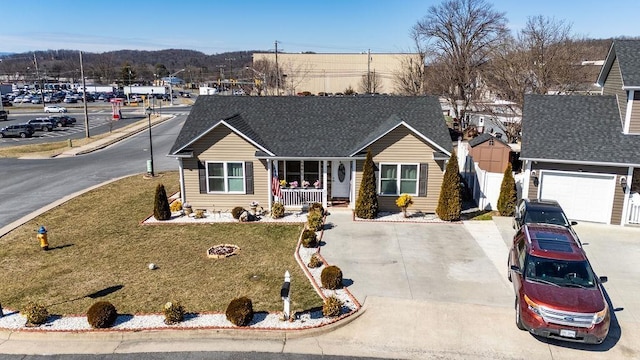 single story home featuring a shingled roof, concrete driveway, covered porch, a front yard, and fence