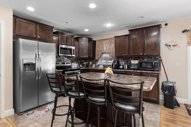 kitchen with dark brown cabinetry, a breakfast bar area, appliances with stainless steel finishes, a center island, and backsplash