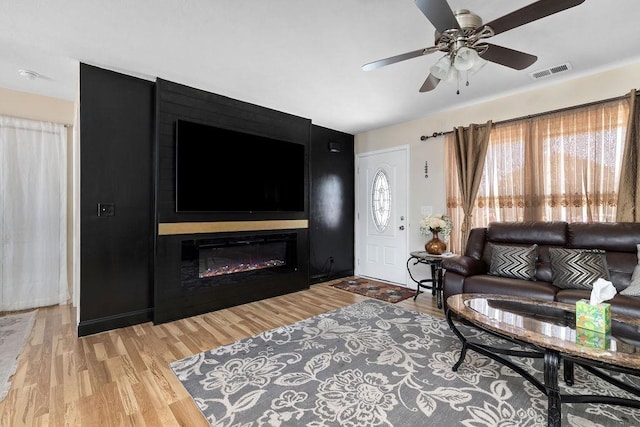 living area featuring a ceiling fan, visible vents, a fireplace, and light wood finished floors