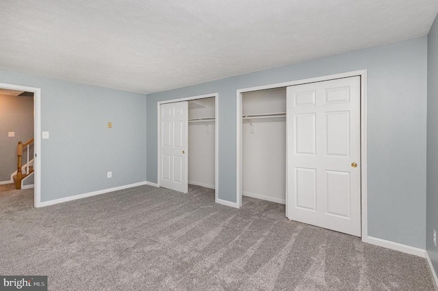 unfurnished bedroom featuring carpet floors, two closets, and baseboards