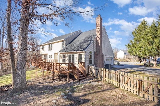 back of property featuring cooling unit, fence, driveway, a wooden deck, and a chimney