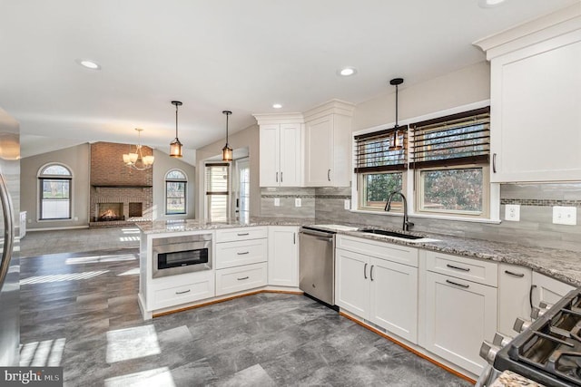 kitchen featuring appliances with stainless steel finishes, open floor plan, white cabinetry, pendant lighting, and a sink