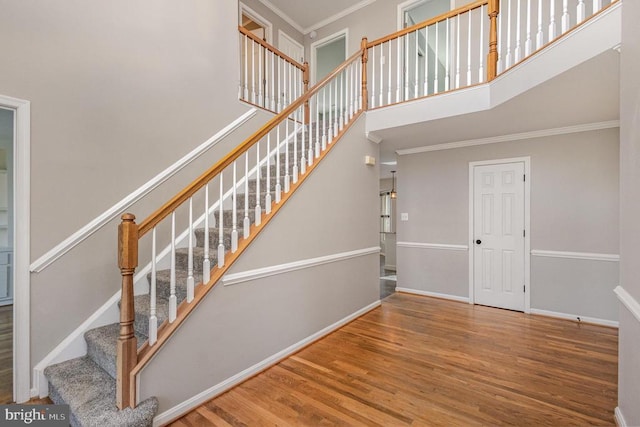 staircase featuring ornamental molding, a towering ceiling, baseboards, and wood finished floors