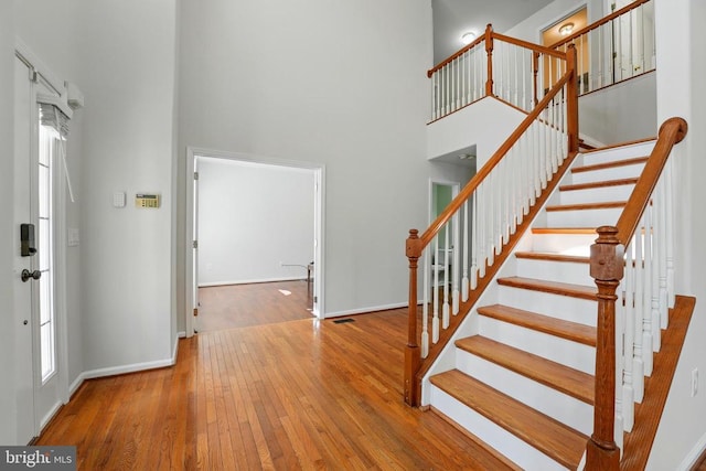 stairway with a healthy amount of sunlight, baseboards, hardwood / wood-style flooring, and a towering ceiling