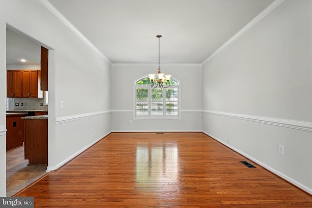 unfurnished dining area featuring an inviting chandelier, crown molding, wood finished floors, and visible vents
