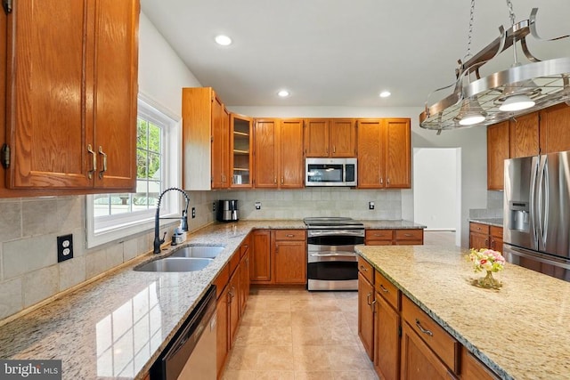 kitchen featuring brown cabinets, a sink, light stone counters, glass insert cabinets, and stainless steel appliances
