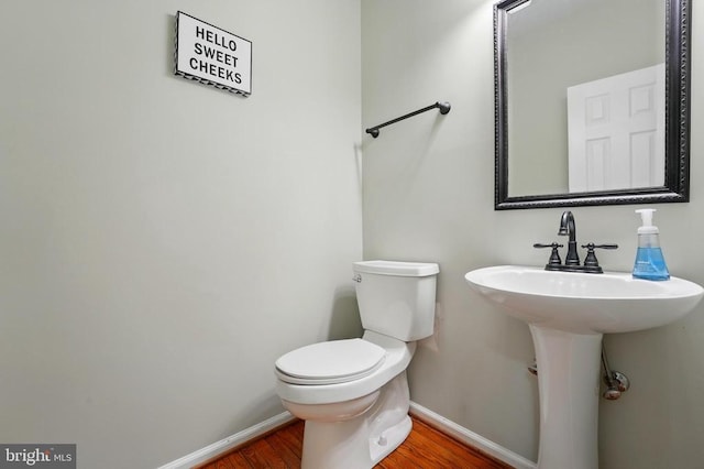 half bath featuring baseboards, toilet, and wood finished floors